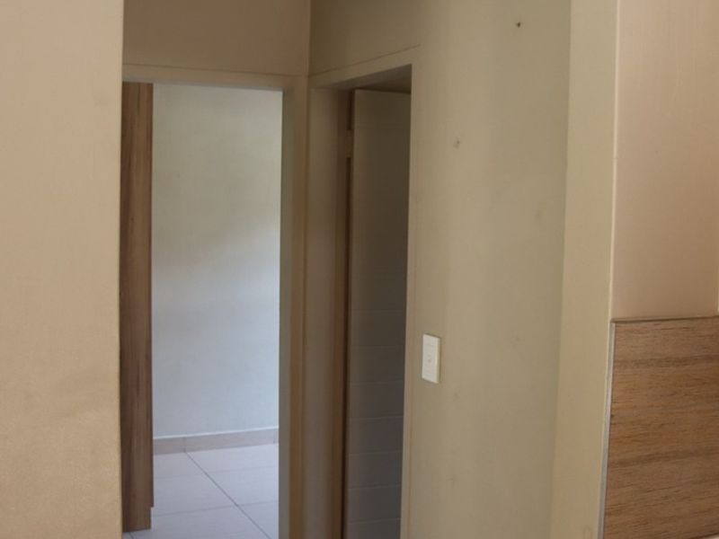 A neutral-toned hallway featuring tiled flooring and cornice detailing, providing access to adjacent rooms within the apartment.