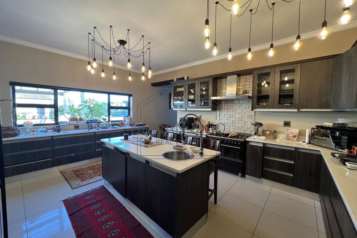 Modern kitchen featuring dark wood cabinetry, a central island with a prep sink, stone countertops, and decorative tiled backsplash with integrated stainless steel appliances.