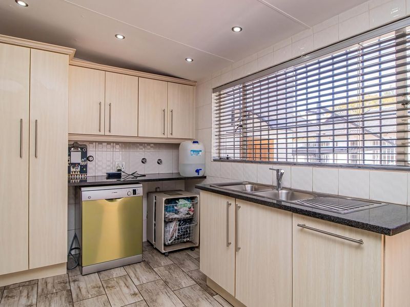 A functional scullery featuring light wood-finish cabinetry, dark laminate countertops, a stainless steel double sink, and tiled splashbacks with recessed lighting.