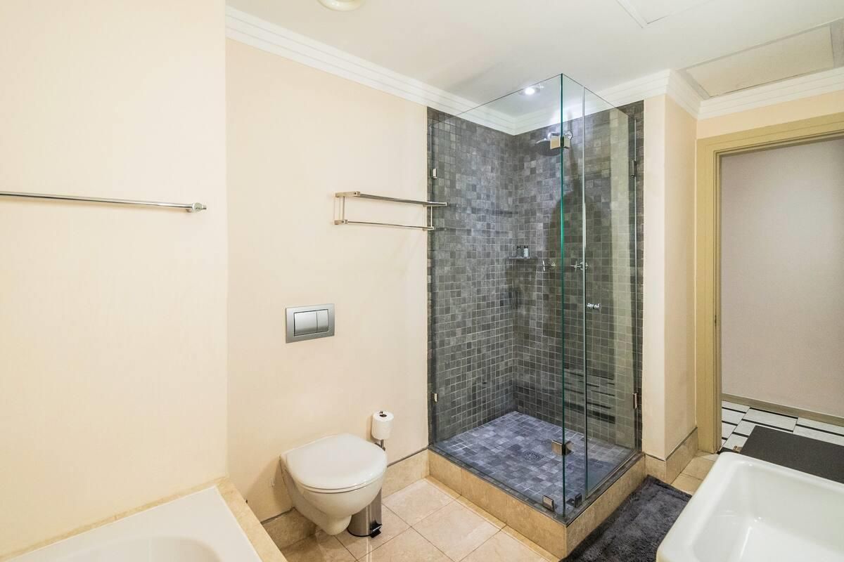 Modern bathroom featuring a glass-enclosed shower with mosaic tiling, a wall-mounted toilet, and a built-in bathtub with neutral finishes.