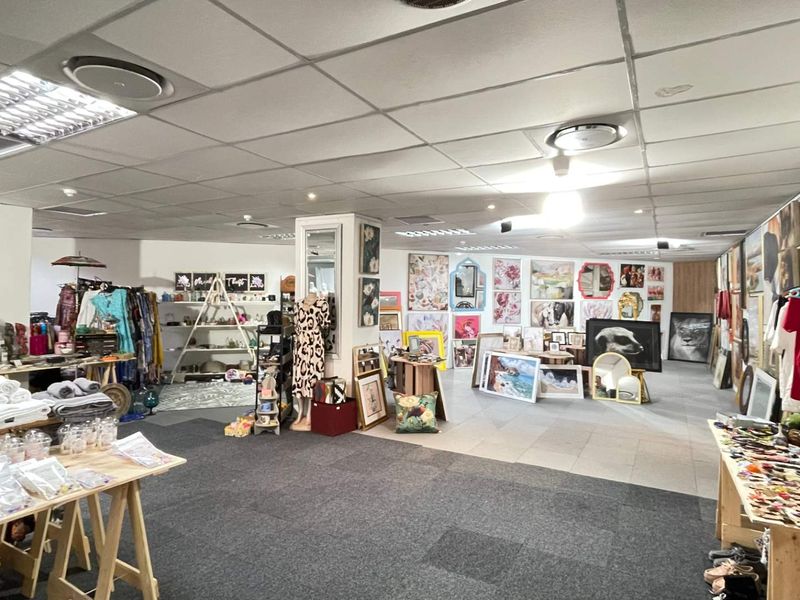 Spacious open-plan retail area featuring a suspended ceiling with recessed lighting, a mix of carpet and tile flooring, and a central structural pillar.