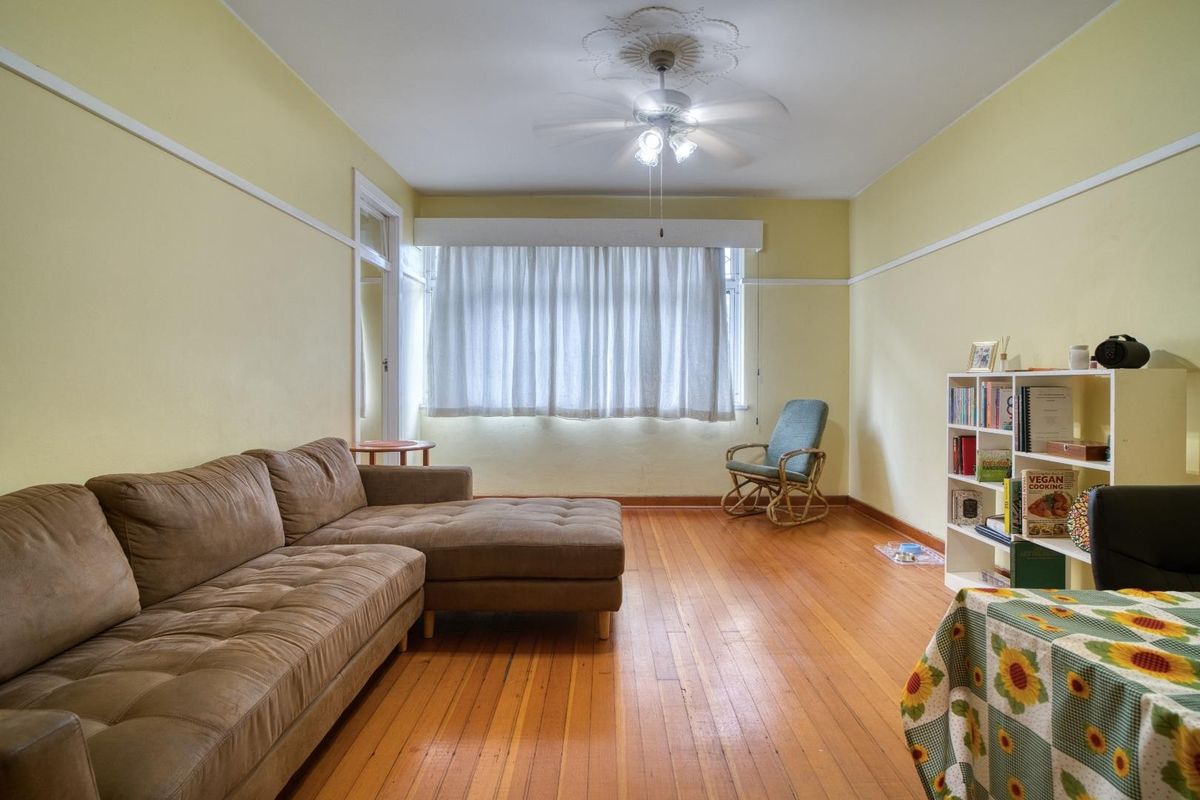 A living room featuring original hardwood flooring, a ceiling fan with decorative rose, and classic picture rail molding.