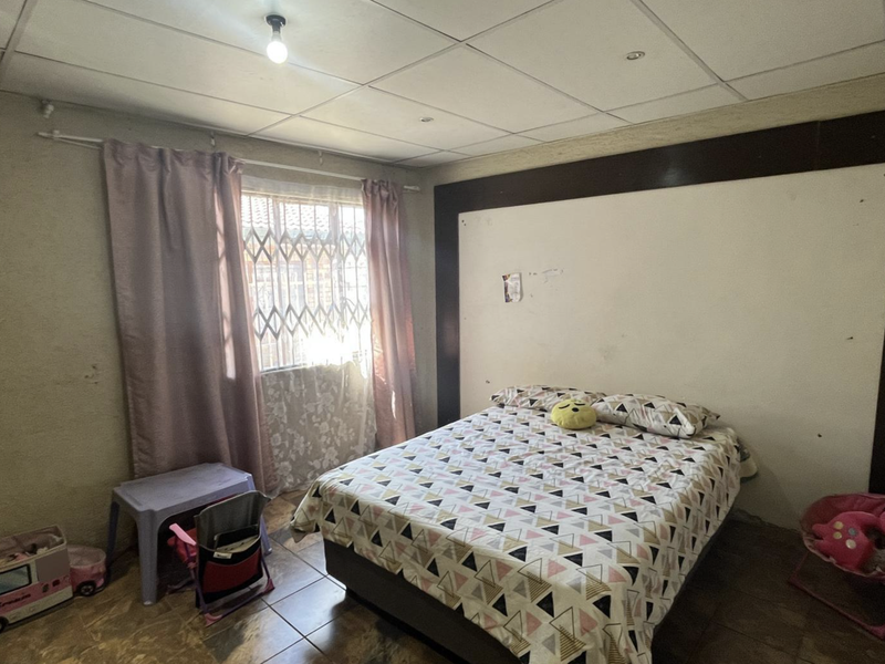 A bedroom featuring tiled flooring, a drop ceiling, and a built-in headboard feature, requiring cosmetic updates to improve its overall condition.