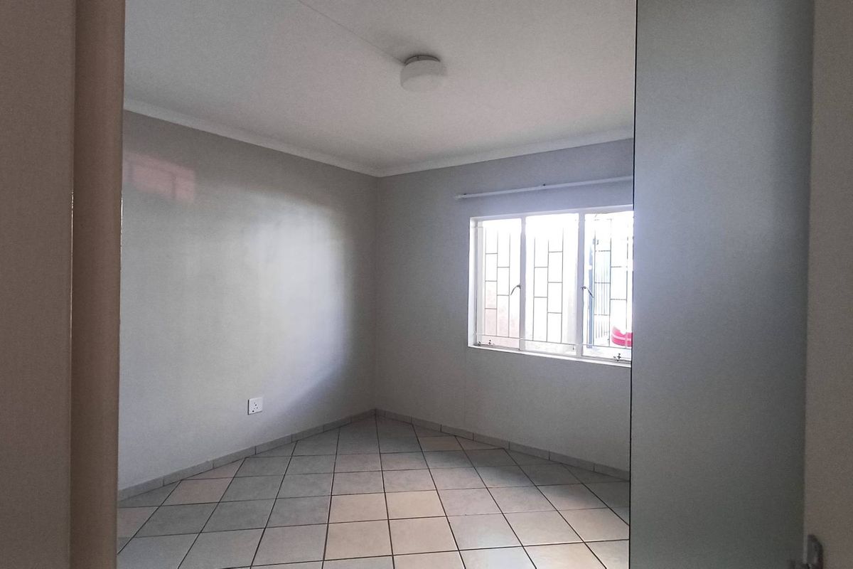 A clean, empty bedroom featuring neutral wall paint, tiled flooring, and a window fitted with security bars.