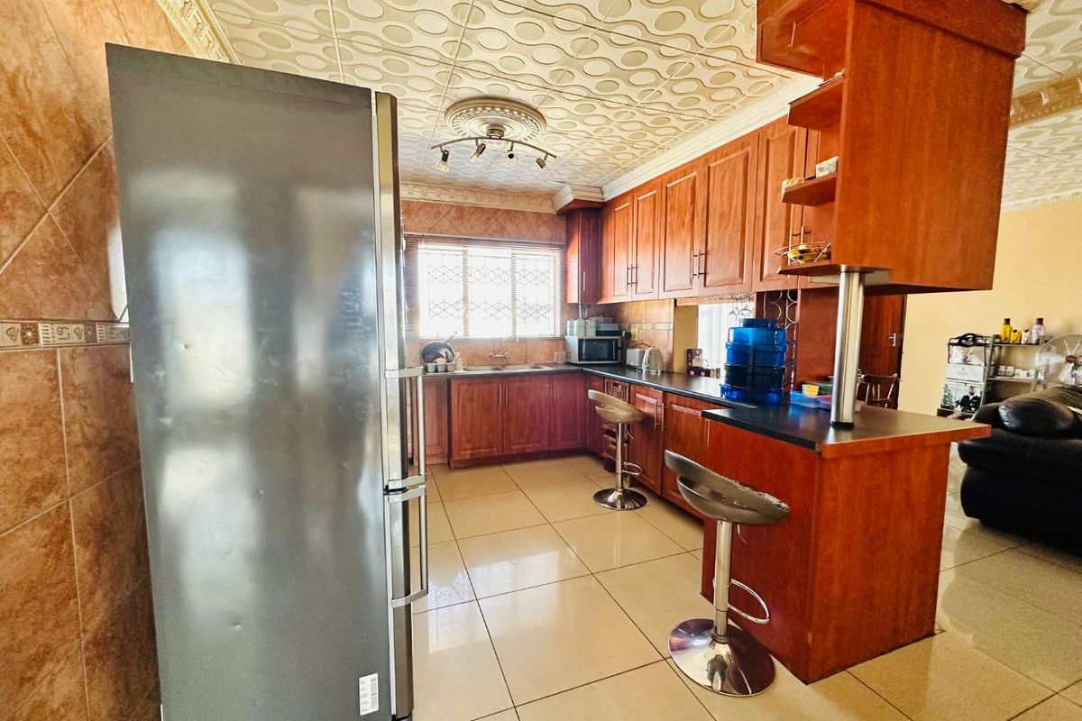 A functional kitchen featuring wooden cabinetry, a breakfast bar, tiled flooring, and decorative ceiling tiles, offering a traditional layout with ample storage space.