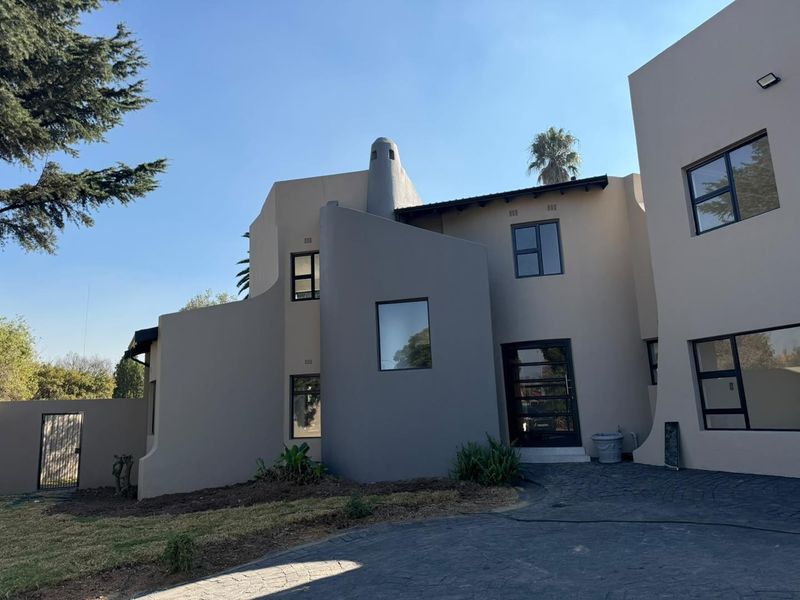 Modern architectural front facade featuring a paved driveway, clean lines, and dark aluminium window frames.
