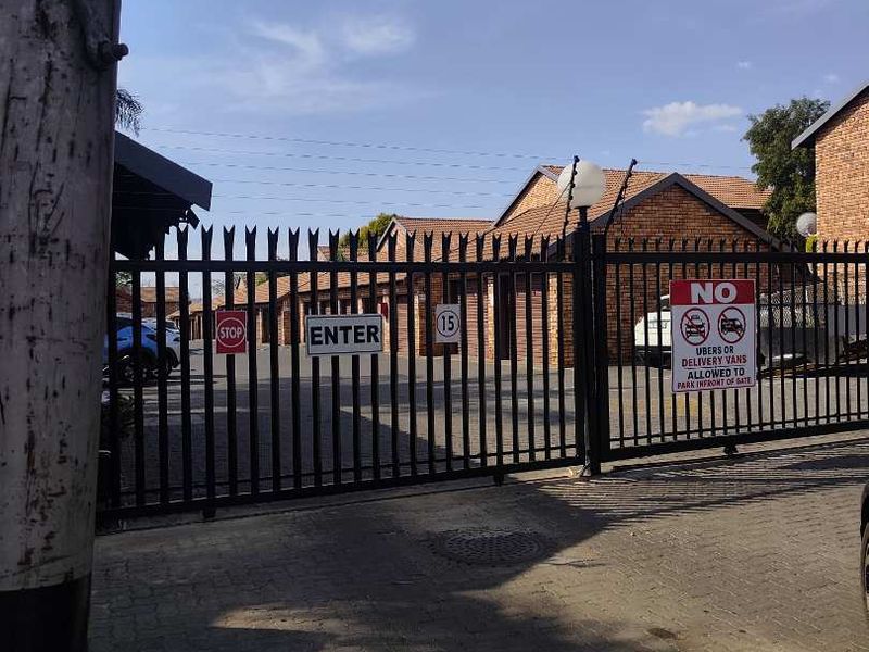 View of the townhouse complex entrance featuring a secure metal gate, paved driveway, and brick building facades.