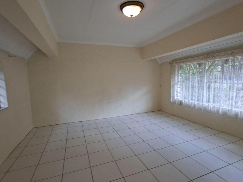 A vacant bedroom featuring neutral tiled flooring, large windows with security bars, and a simple flush mount ceiling light fixture.