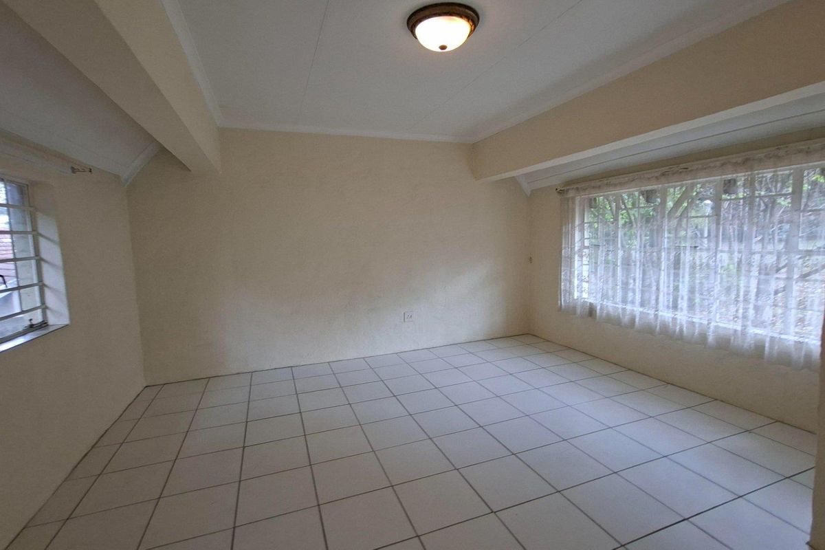 A vacant bedroom featuring neutral tiled flooring, large windows with security bars, and a simple flush mount ceiling light fixture.