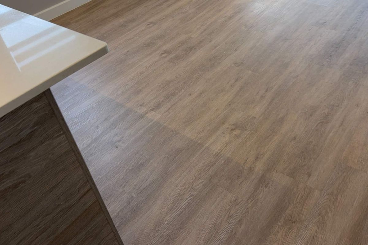 A close-up view of modern wood-look laminate flooring and a portion of a kitchen island with a stone benchtop.