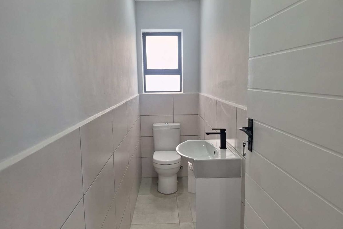 A compact guest bathroom featuring modern floor-to-ceiling wall tiles, a sleek pedestal basin with a black mixer tap, and a standard toilet.