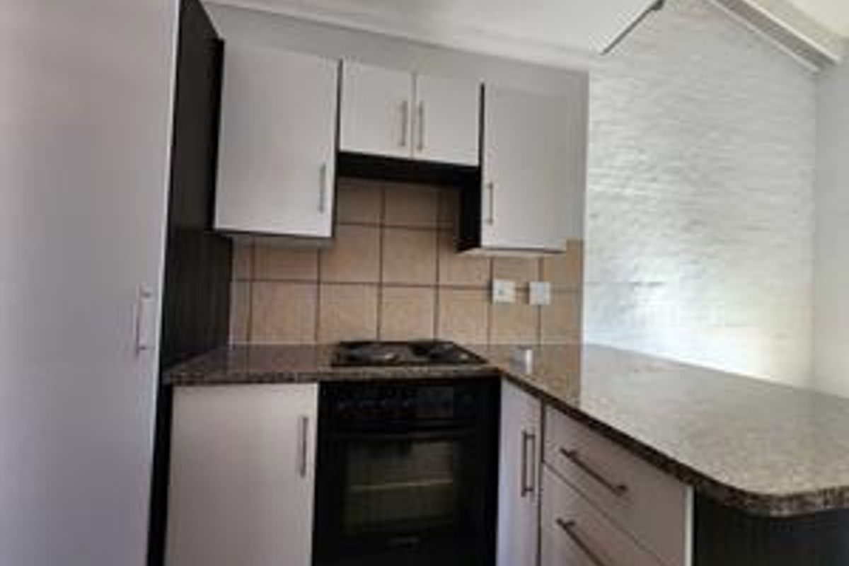 Compact kitchen featuring modern white cabinetry, granite countertops, a tiled backsplash, and a built-in oven with hob, complete with a functional breakfast bar.