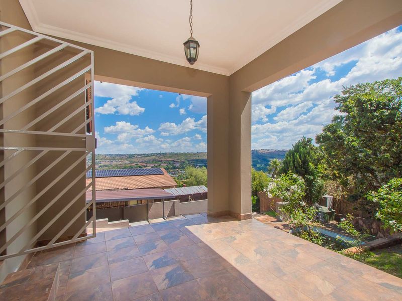 A covered patio featuring tiled flooring and a security gate, offering expansive elevated views of the surrounding landscape.