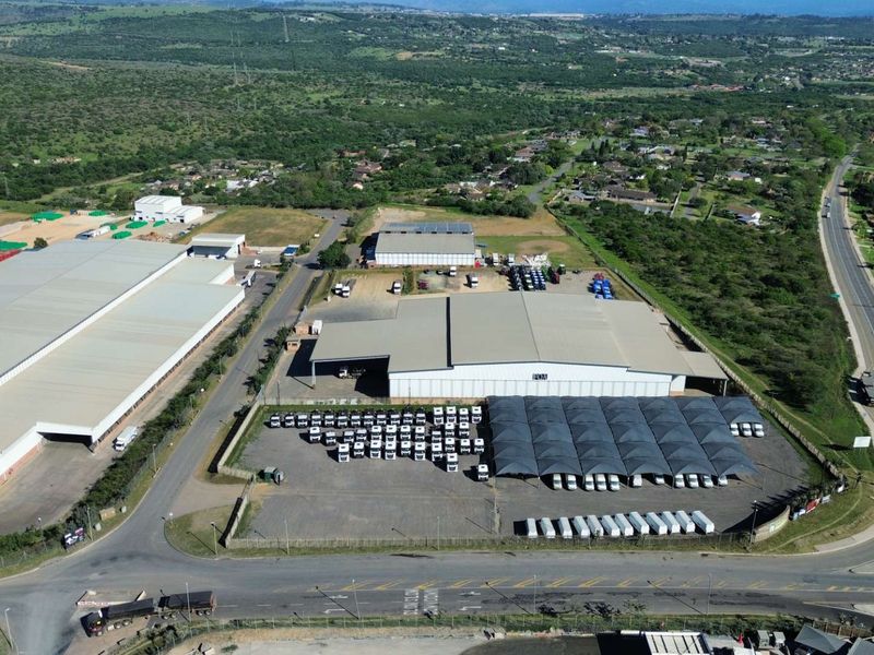 Aerial view of an industrial property featuring large warehouse facilities, extensive paved parking areas with shade structures, and direct road access.