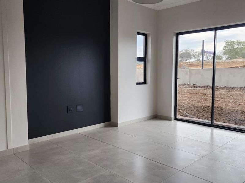 A bright, empty living room featuring large sliding glass doors, modern tiled flooring, and a striking black accent wall.