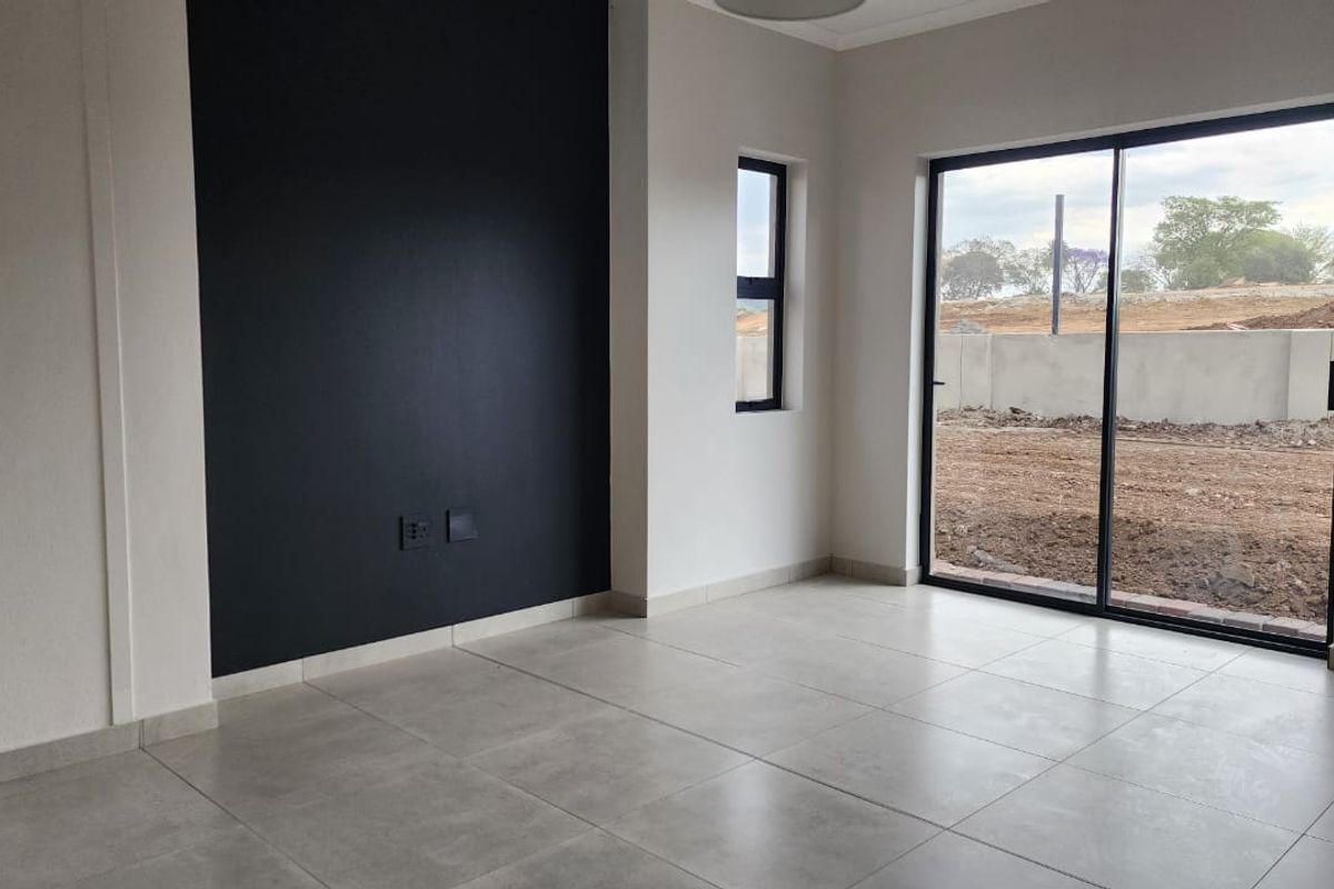 A bright, empty living room featuring large sliding glass doors, modern tiled flooring, and a striking black accent wall.