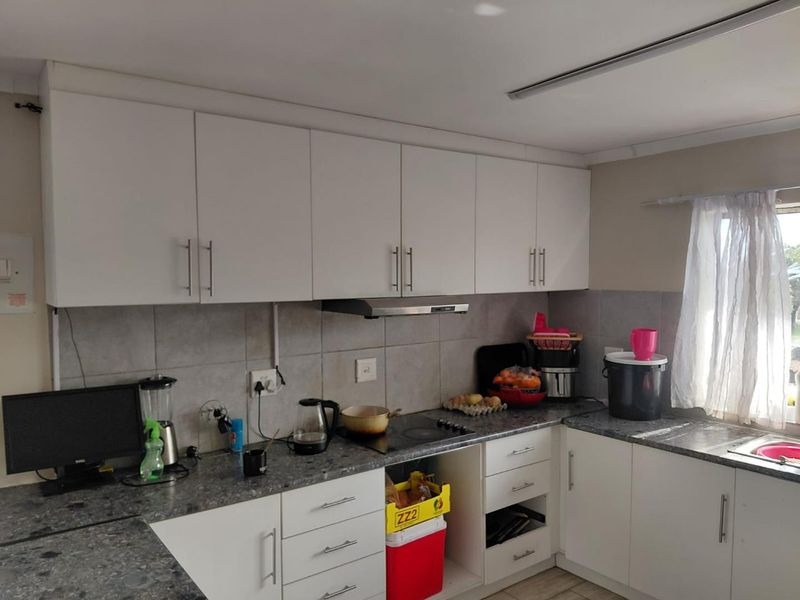 A functional kitchen featuring white cabinetry, grey laminate countertops, a tiled backsplash, and an integrated extractor fan.