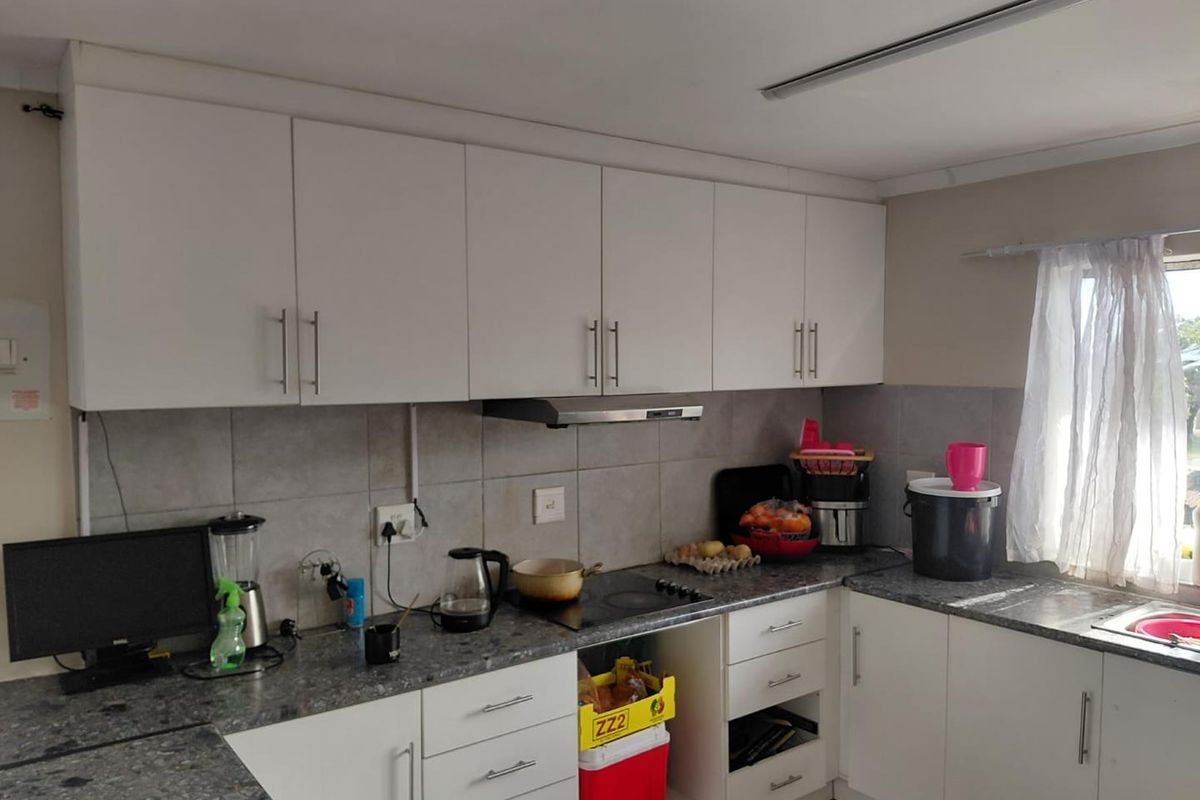 A functional kitchen featuring white cabinetry, grey laminate countertops, a tiled backsplash, and an integrated extractor fan.