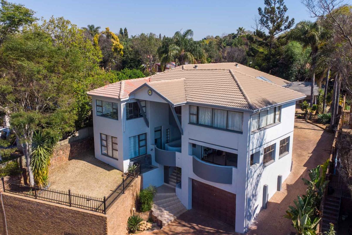 Aerial view of a multi-level residential property featuring a tiled roof, concrete driveway, and established garden surroundings.