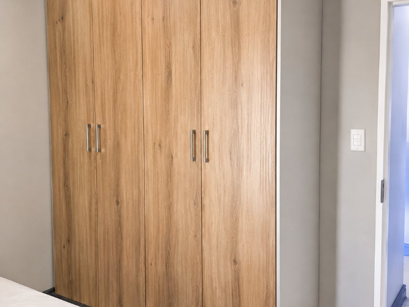A well-maintained bedroom featuring modern wood-finish built-in wardrobes and neutral tiled flooring.