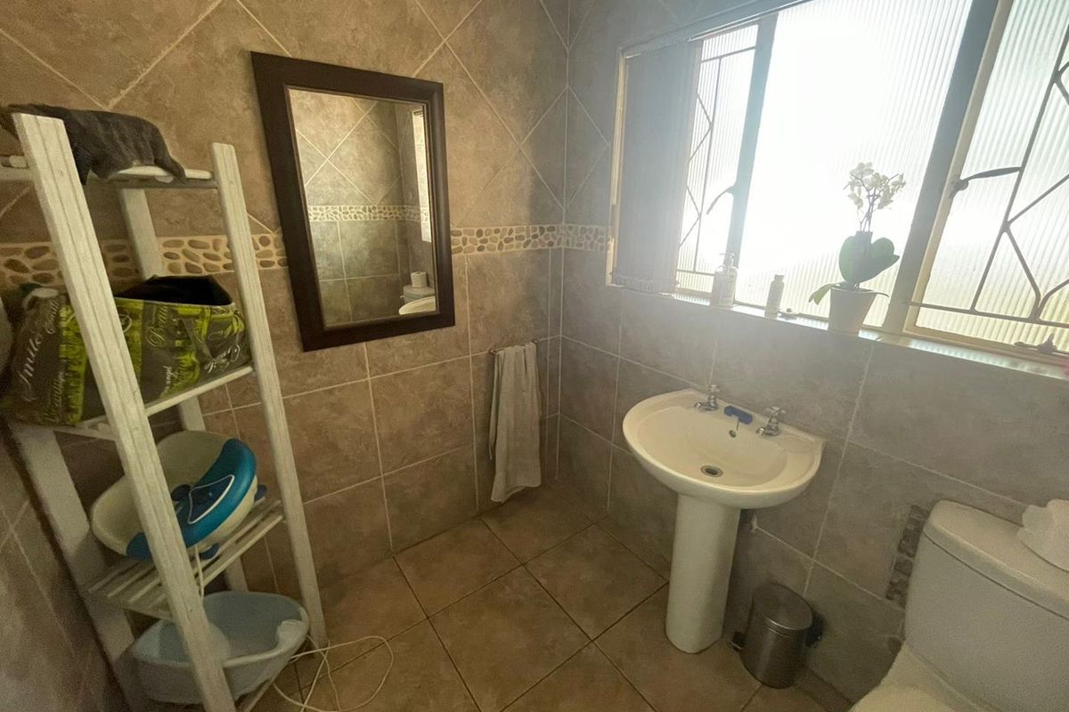 A functional bathroom featuring floor-to-ceiling tiled walls, a pedestal basin, and a toilet, with natural light provided by a large window.