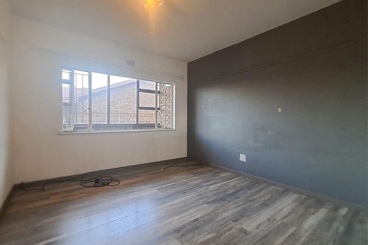 An empty bedroom featuring wood-look laminate flooring, a large window with security bars, and a dark grey feature wall.