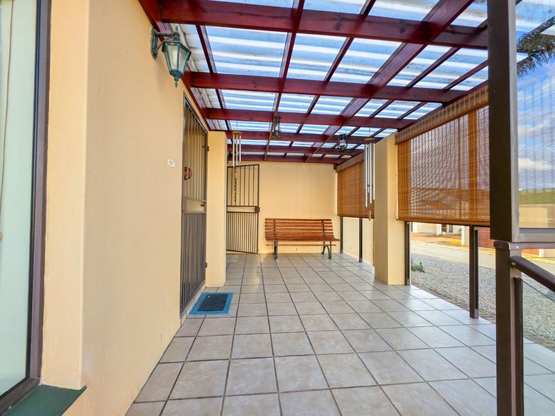 A covered patio area featuring a timber pergola with translucent roofing, tiled flooring, and integrated security gates, providing a functional outdoor entertainment space.