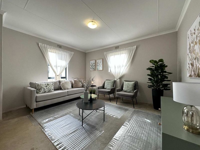 A well-maintained living room featuring neutral wall tones, classic ceiling cornicing, and dual windows that provide ample natural light.