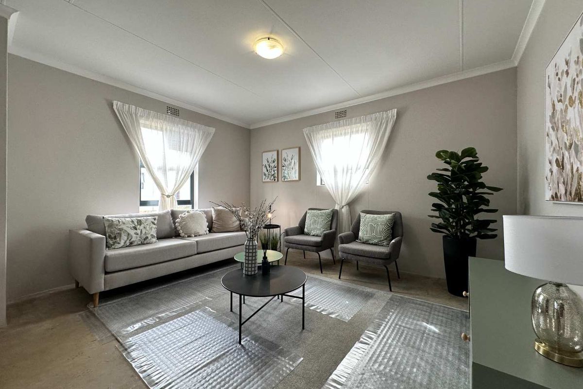 A well-maintained living room featuring neutral wall tones, classic ceiling cornicing, and dual windows that provide ample natural light.