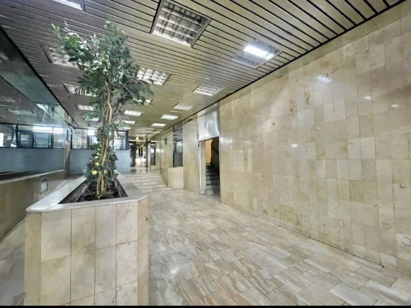 Spacious apartment building entrance lobby featuring marble wall and floor finishes, a built-in planter, and a suspended metal ceiling with recessed lighting.