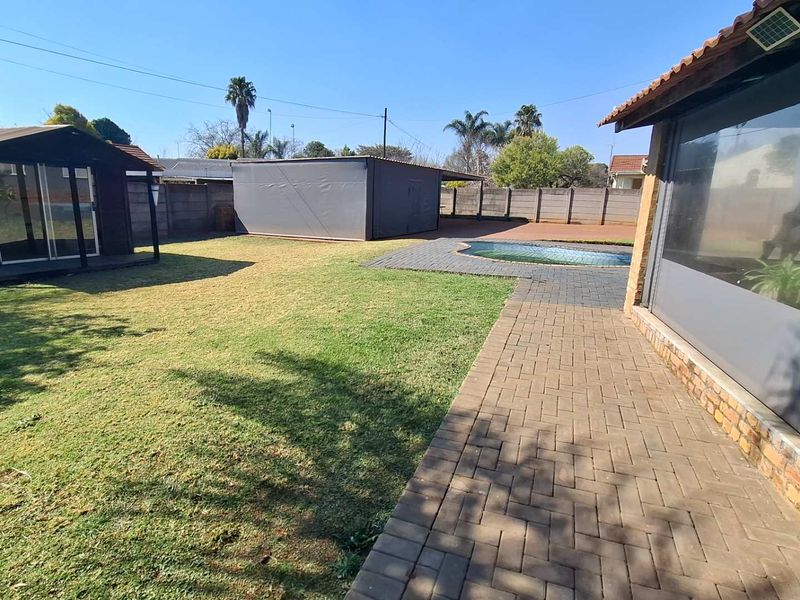 Spacious rear garden featuring a swimming pool, paved patio area, and a detached outbuilding, enclosed by a perimeter boundary wall.