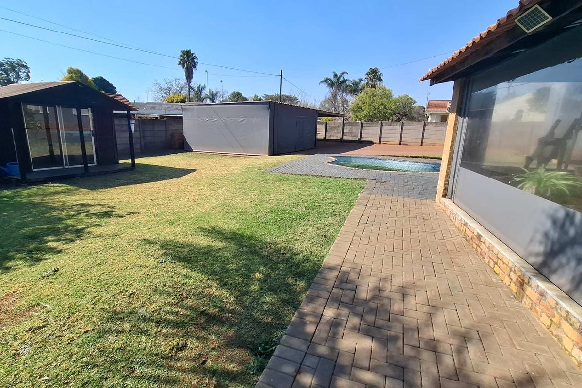 Spacious rear garden featuring a swimming pool, paved patio area, and a detached outbuilding, enclosed by a perimeter boundary wall.