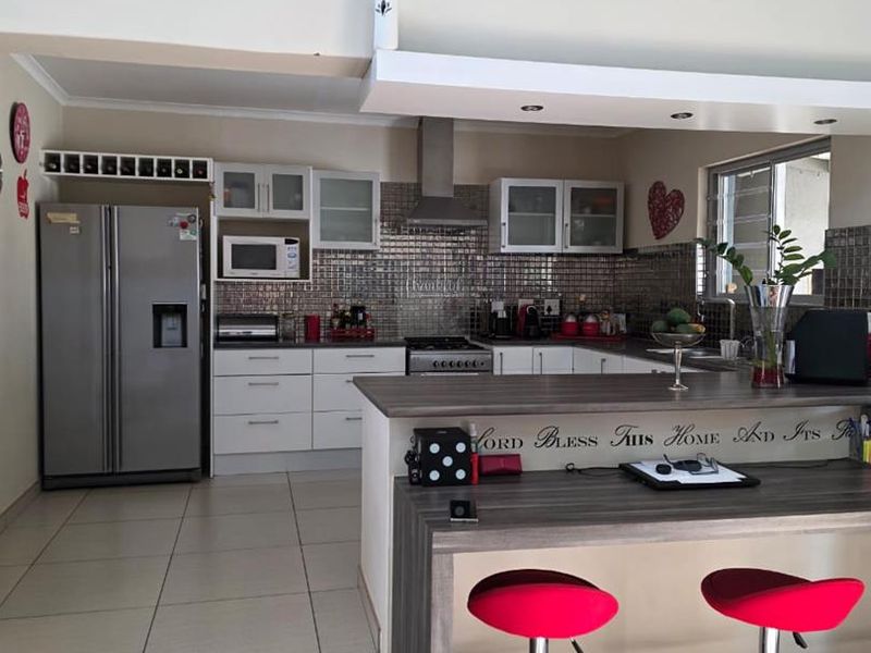 A functional kitchen featuring modern cabinetry, a stainless steel extractor fan, tiled splashback, and a convenient breakfast bar area with tiled flooring.