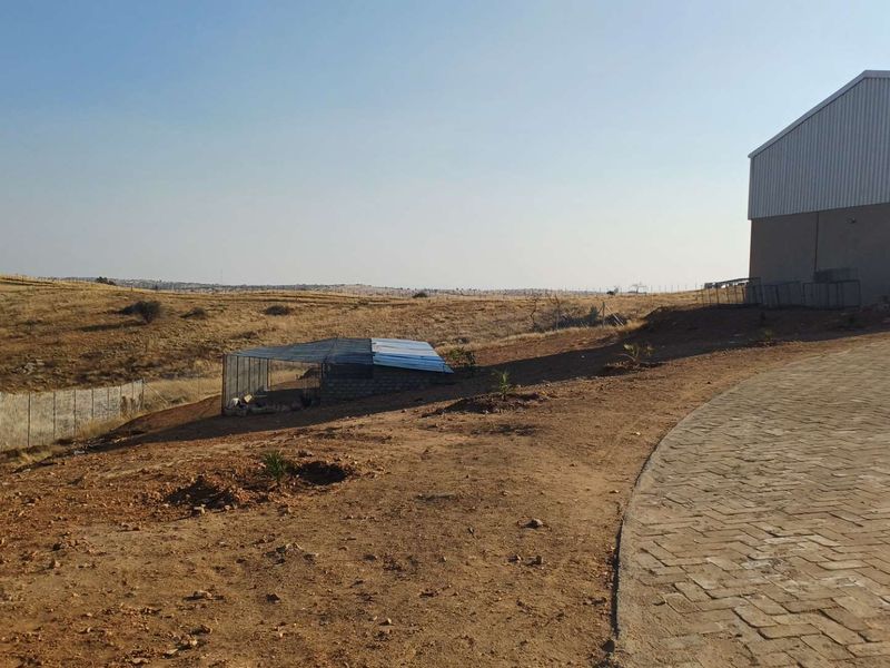 A view of the farm property featuring a paved driveway, a large metal shed, and expansive open land with wire fencing.