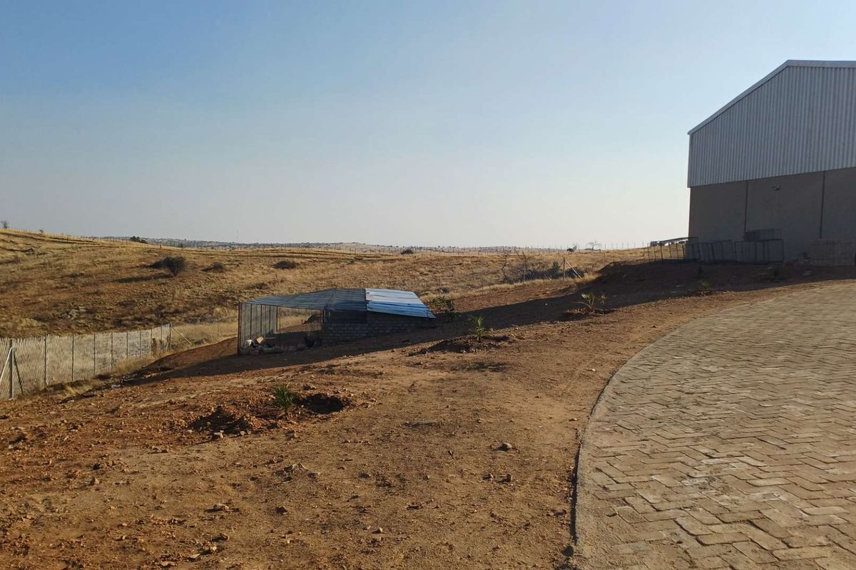 A view of the farm property featuring a paved driveway, a large metal shed, and expansive open land with wire fencing.