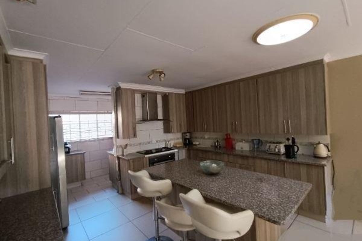 A functional kitchen featuring wood-finish cabinetry, granite countertops, a central island with seating, and tiled flooring.