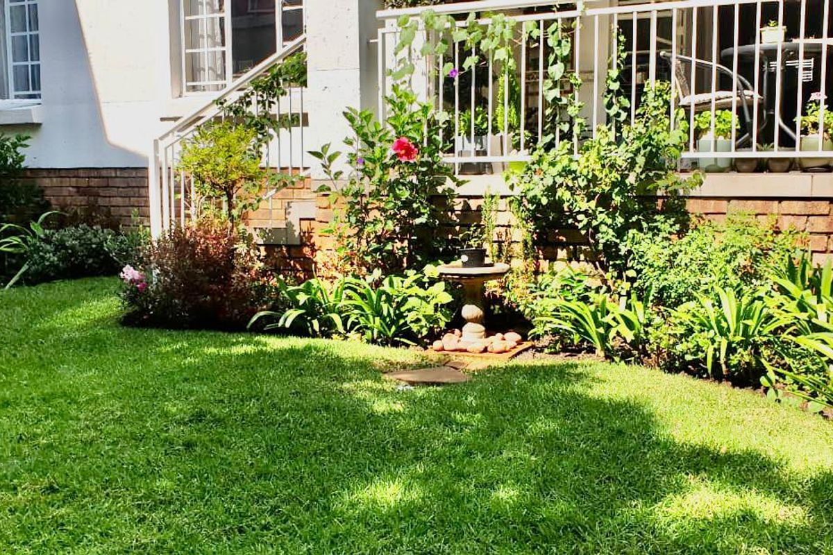 A well-maintained rear garden featuring a lush lawn, established garden beds, and a raised patio area with white metal railings.