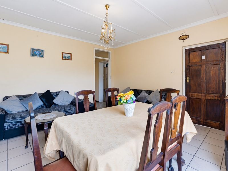 A living and dining area featuring tiled flooring, a timber door, and a central ceiling light fixture.