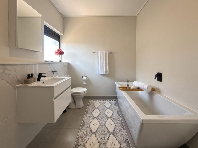 Modern bathroom featuring a wall-mounted vanity, sleek bathtub, contemporary matte black fixtures, and elegant marble-look wall tiling.