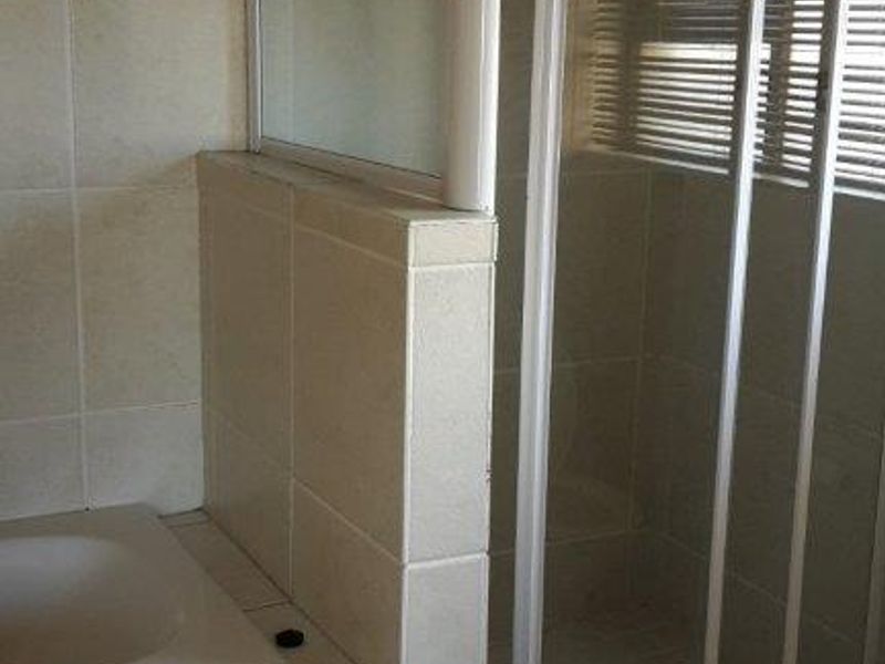 A functional bathroom featuring a built-in bathtub and a separate shower enclosure with tiled finishes throughout.