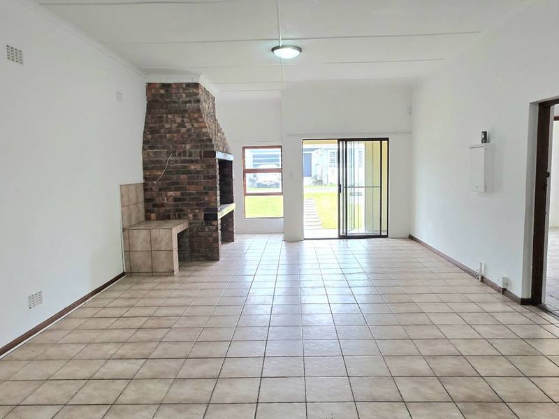 Spacious, empty living area featuring tiled flooring and a prominent built-in brick fireplace, with direct access to the rear garden through a sliding door.