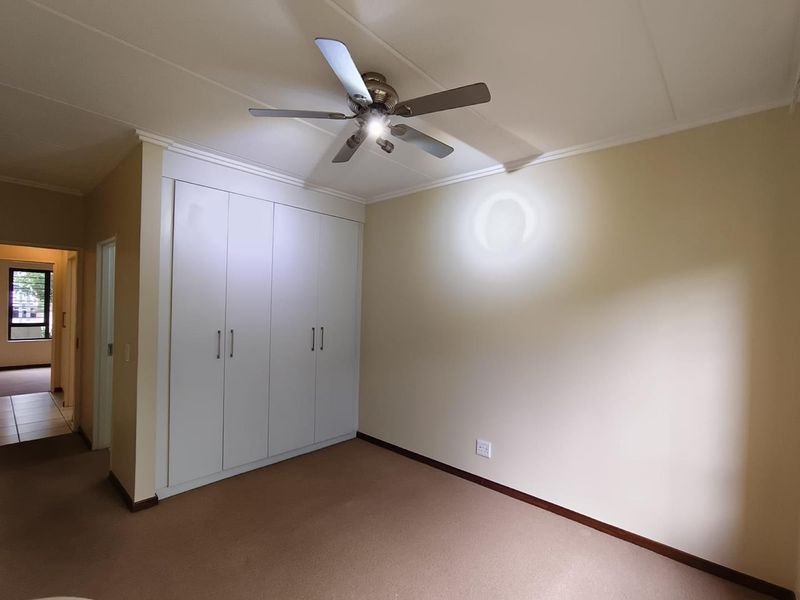 A clean, empty bedroom featuring neutral walls, carpeted flooring, built-in cupboards, and a ceiling fan.