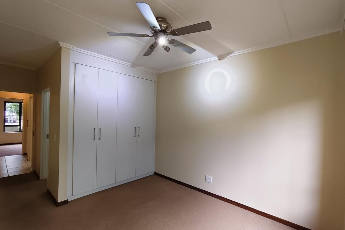 A clean, empty bedroom featuring neutral walls, carpeted flooring, built-in cupboards, and a ceiling fan.
