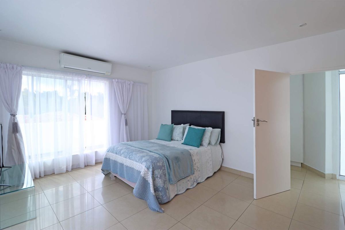 A bright and spacious bedroom featuring neutral tiled flooring, a wall-mounted air conditioning unit, and large windows allowing for ample natural light.
