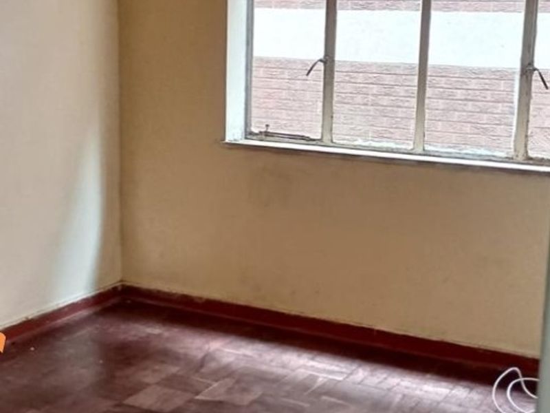 An empty bedroom featuring original parquet flooring and a large metal-framed window, offering a blank canvas for renovation.