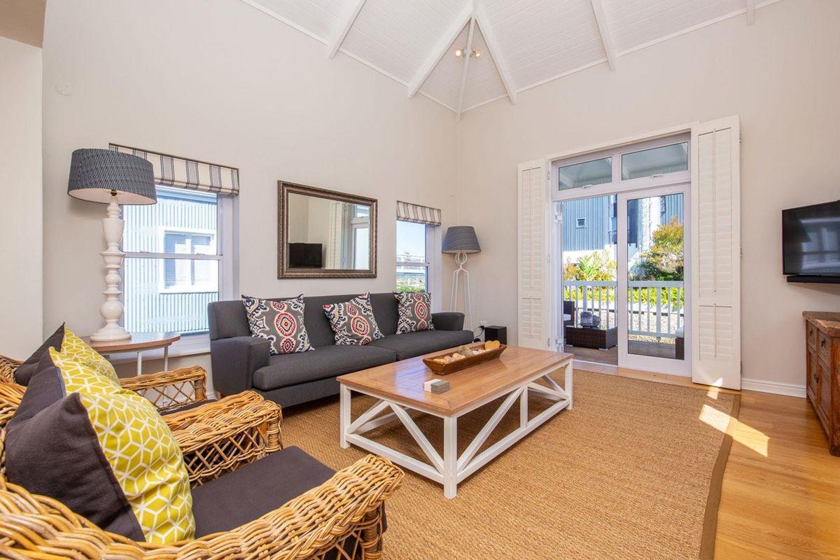 Bright living room featuring high vaulted ceilings, timber flooring, and direct access to an outdoor balcony through glass doors.