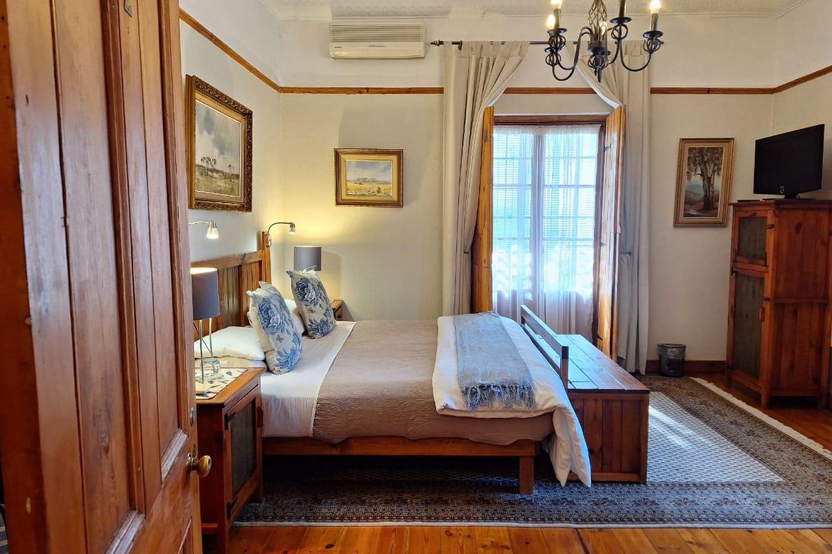 A well-maintained bedroom featuring polished timber flooring, ornate ceiling detailing, a wall-mounted air conditioning unit, and classic French doors leading to the exterior.