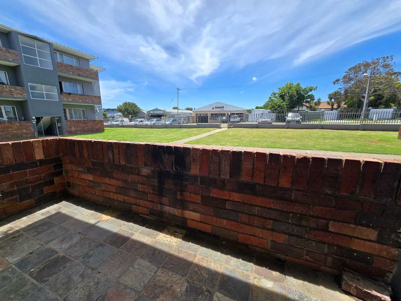 A private balcony featuring a brick balustrade and stone tile flooring, overlooking a communal lawn area.