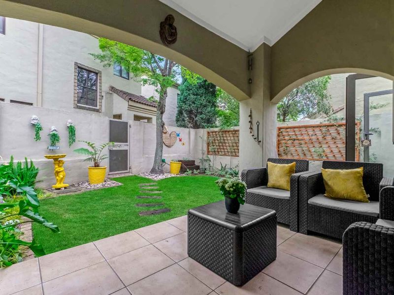 A covered patio area featuring tiled flooring and an archway, overlooking a private garden with a lawn and established greenery.