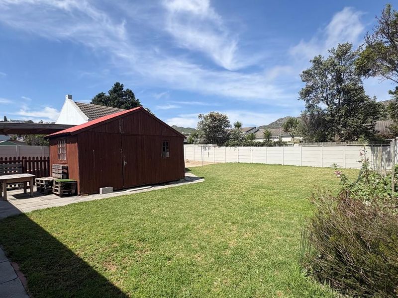 Spacious rear garden featuring a well-maintained lawn, paved patio area, and a detached timber storage shed enclosed by perimeter boundary walls.